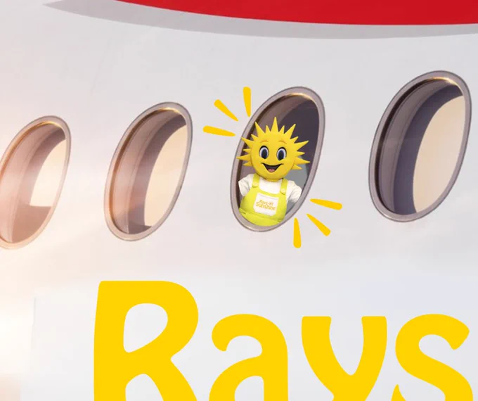 Close up shot of the side of a plane - with Sunny the yellow Rays of Sunshine mascot in view in one of the windows. The Rays of Sunshine logo is cut off in the bottom right hand corner. 