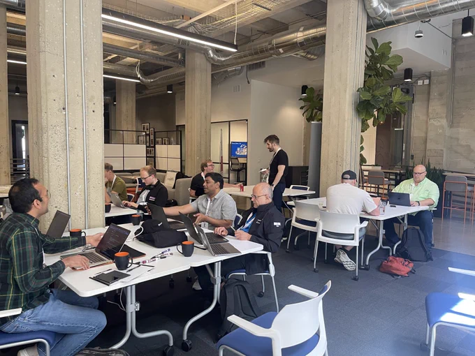 CommCon hackathon in progress with attendees sat at tables working on laptops and chatting