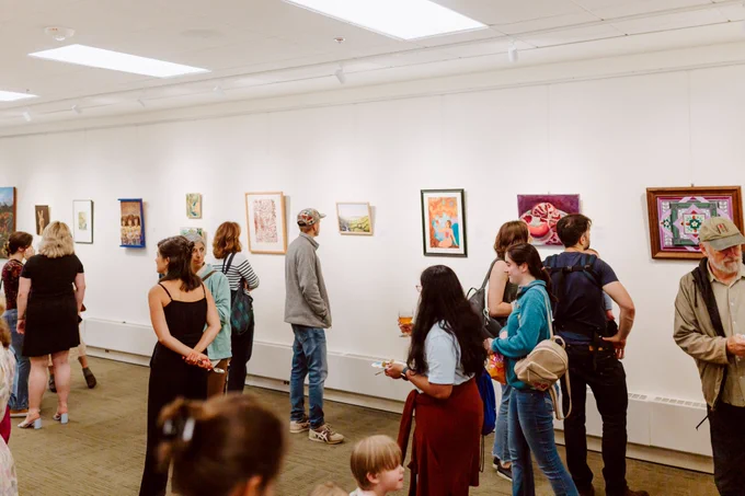 A number of people in an art gallery, talking or checking out the work on display.