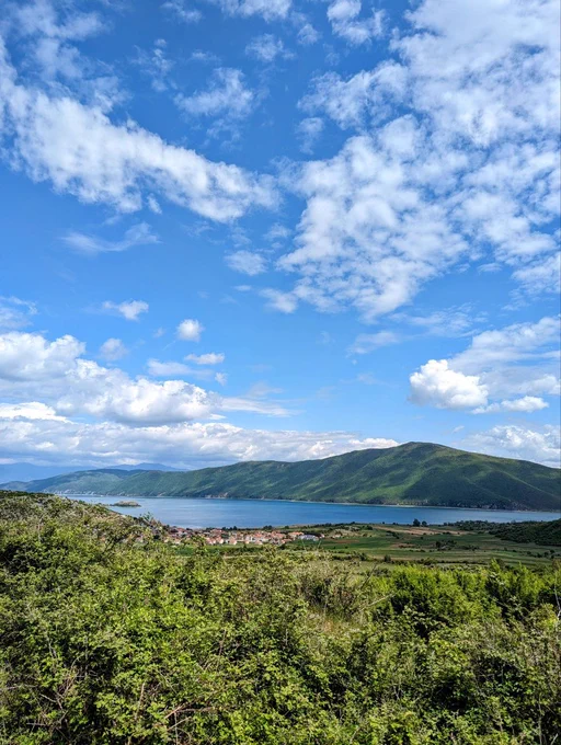 A view of lake Prespa with a mountain, a small island, a village and a forest.