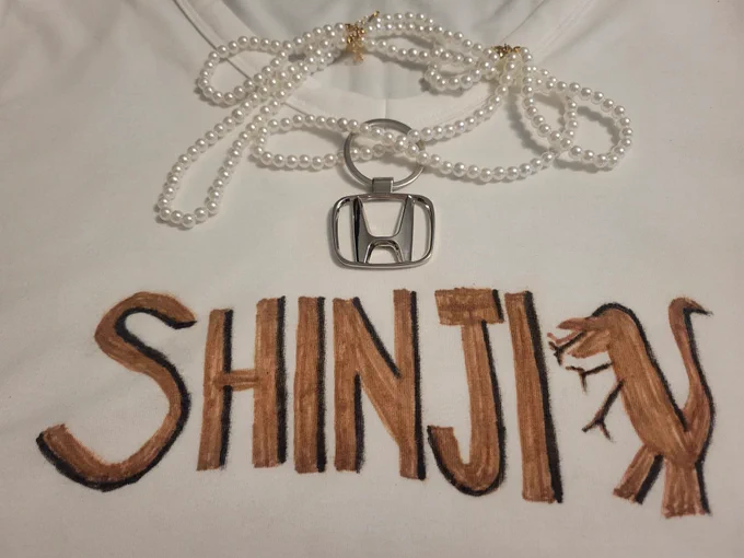 White tshirt with SHINJI written in brown marker. A pearl necklace with a Honda logo.