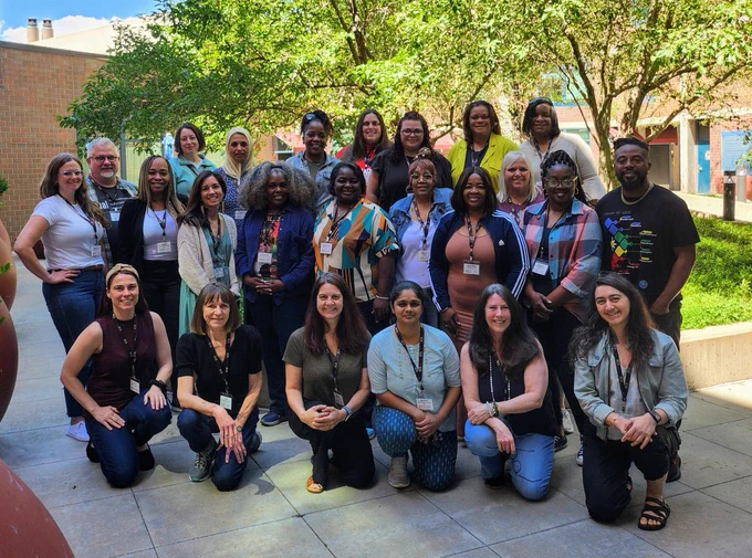A diverse group of 24 ECS teachers and staff outside on a sunny day with a tree behind them