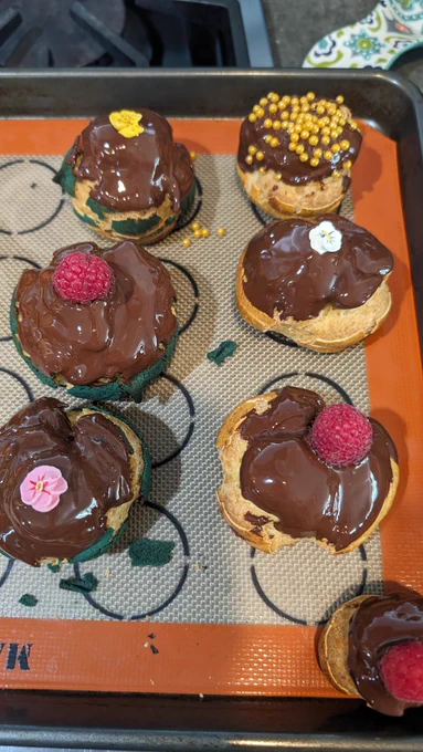 6 chocolate coated cream puffs on a baking sheet.