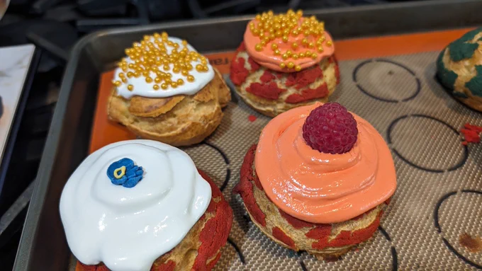 4 decorated cream puffs on a baking sheet.