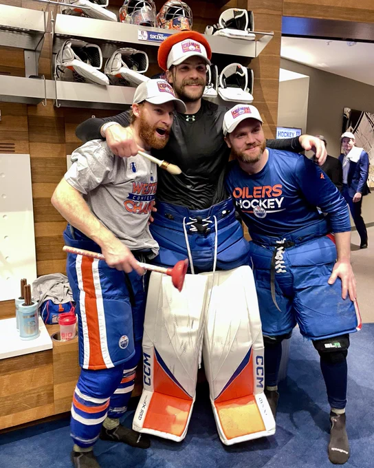 Connor Brown holding the plunger, Stuart Skinner wearing an orange beret, and Calvin Pickard celebrating in the Oilers locker room.