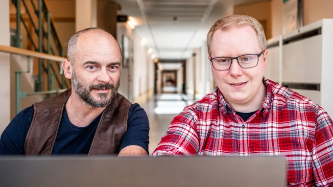 Two men are sitting at a computer.