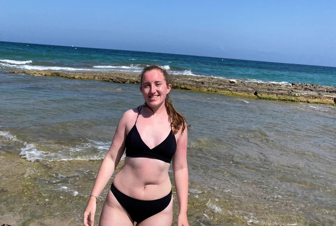 Allie, wearing a bikini, standing in front of the sea.