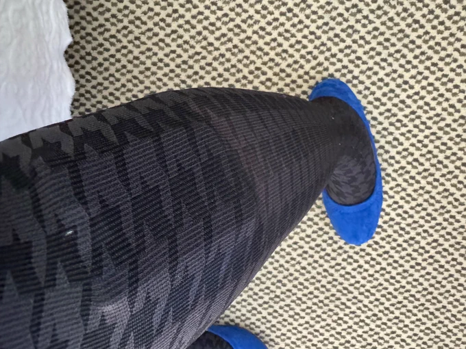 Shiri’s medical device is visible through gray-and-black pantyhose. She is wearing blue flats.
