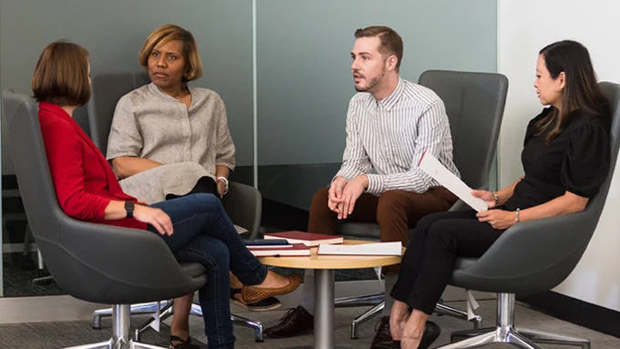 A group of four professionally dressed people talk while sitting around a small table.