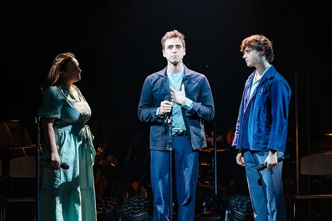 A photo showing three performers on a darkened stage in a spotlight 