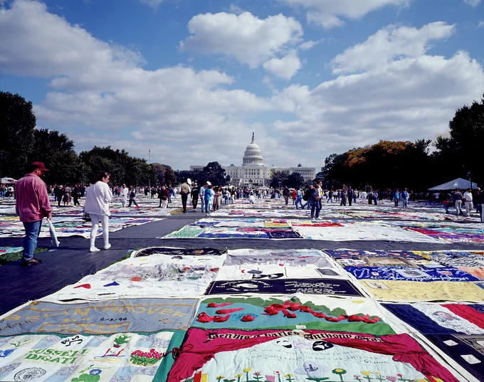 Thousands of colorful squares of fabric covered in names and pictures are laid out in rows on the wide lawn of the National Mall with the white dome of the Capitol in the background.