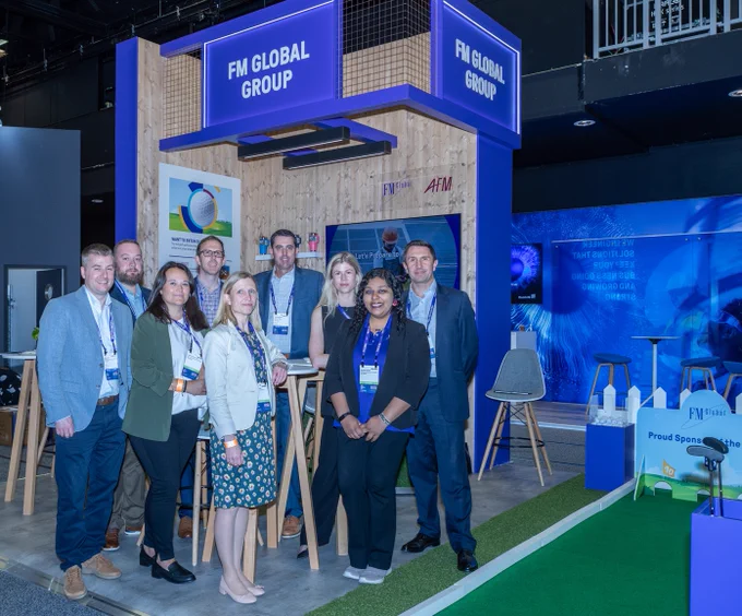 Image of the FM Global team standing on the stand during the Airmic 2024 conference. The stand has a purple banner at the top with the words, "FM Global Group" and the logos for AFM and FM Global underneath. 