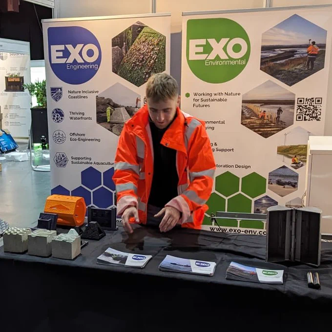 Team member organising an event booth, with information banners, brochures and example models. 