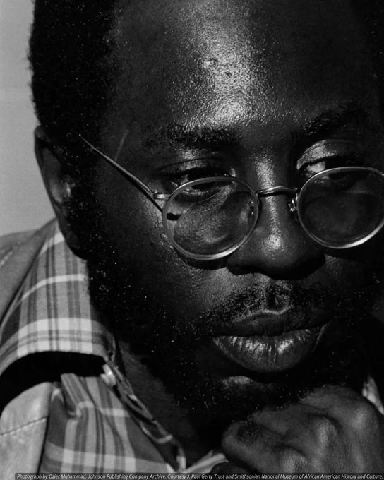 A black-and-white photo of a man (Curtis Mayfield) staring off into the distance. His chin rests on the top of his fist.