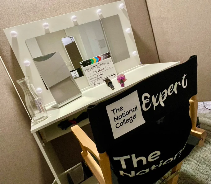 A directors chair in front of a mirror with lightbulbs round it.