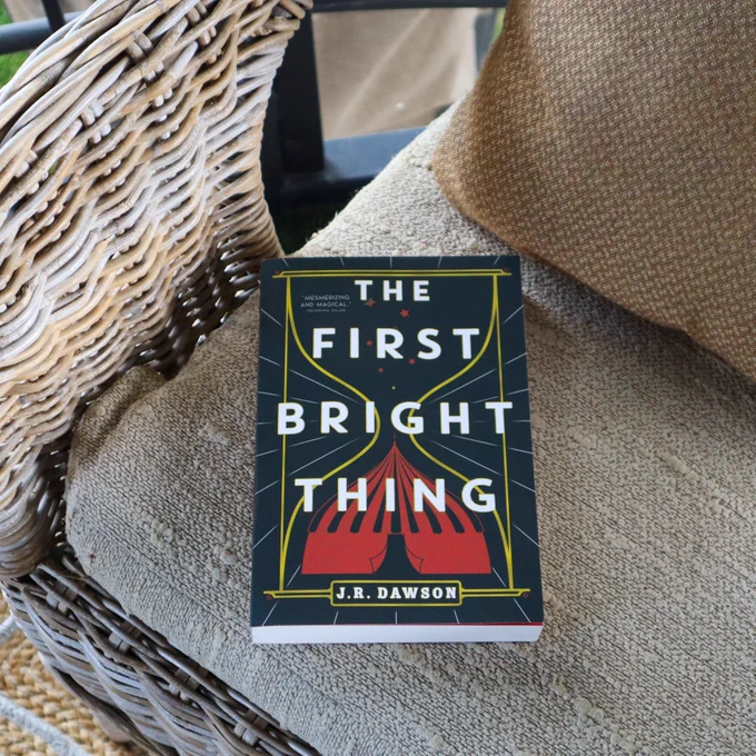 A paperback coipy of The First Bright Thing by J.R. Dawson is laying on a chair 