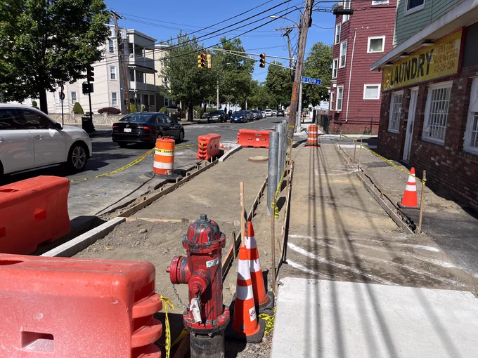 Photo of a sidewalk and cycle track under construction, temporarily as fifty and with assorted cones and barricades. Both are adjacent to motor vehicle lanes.