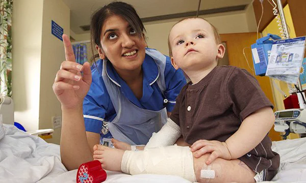 Nurse points upwards as young boy, sitting on hospital bed, looks up too. Photo is intended to show the relationship between nurse and child at its best with the nurse engaging with and distracting the child.