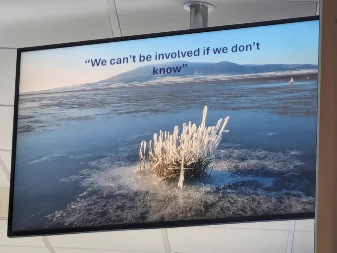 Photo of a screen showing a slide of a frozen seascape with the quote 'We can't be involved if we don't know'
