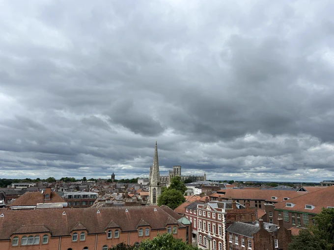 Looking out over the city of York with red topped roofs and a church spire in the middle. The clouds are grey and low hanging.
