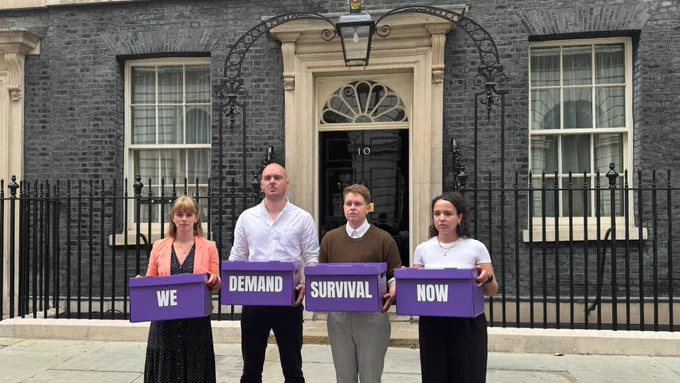 pcuk representatives standing in front of 10 downing street, holding purple petition boxes reading 'we demand survival now'