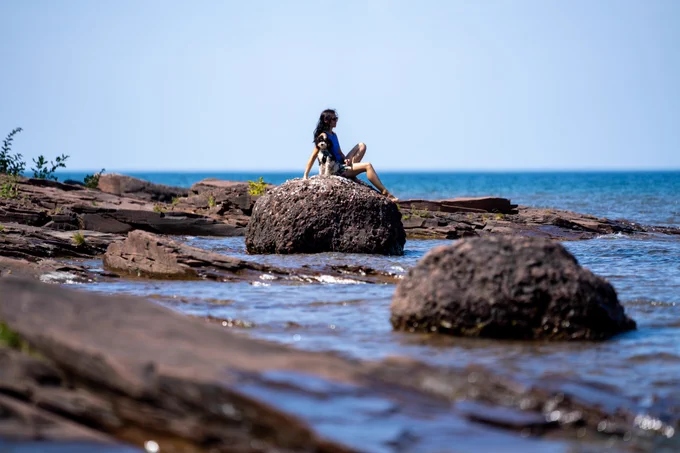 Person sitting on rock with dog on shoreline of Porcupine Mountain State Park. Photo Credit goes to Tyler Leipprandt, Michigan DNR Photo Ambassador.