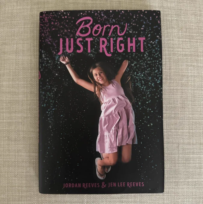 A book titled "Born Just Right" by Jordan Reeves and Jen Lee Reeves, featuring a cover image of a joyful child wearing a pink dress, enthusiastically raising her arms against a purple starry background.