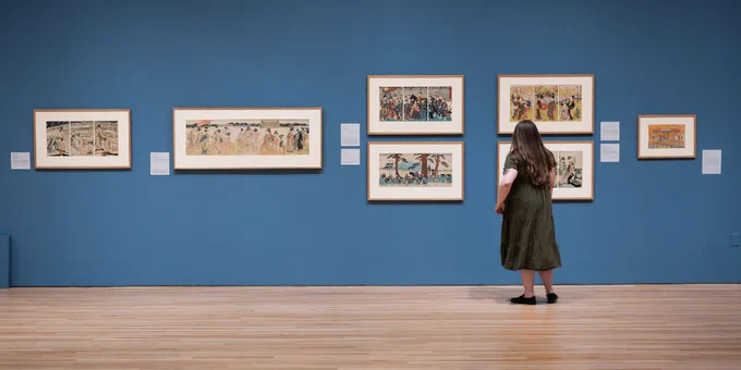 A person looking at several large Japanese woodblock prints on a gallery wall