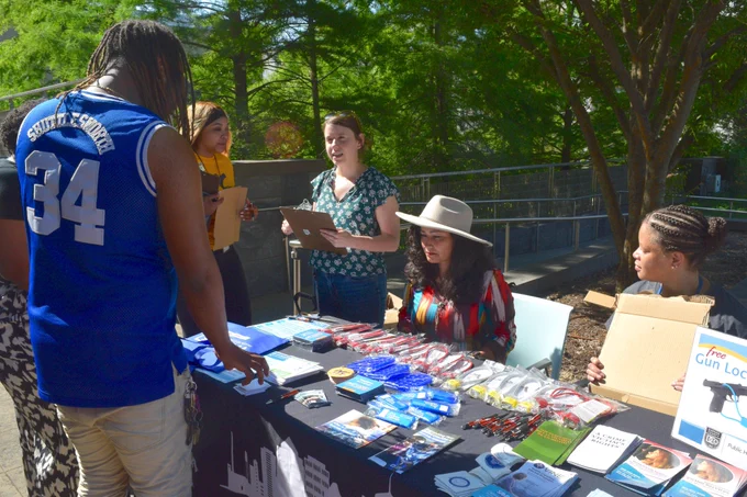A man looking down at a table with gun locks and gun safety information. Four women are also at the table to provide information
