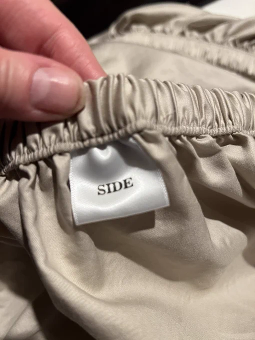 A king size fitted sheet has a soft satin label with the word “side” sewn into the side. The top and bottom of this fitted sheet are labeled “top/bottom”.