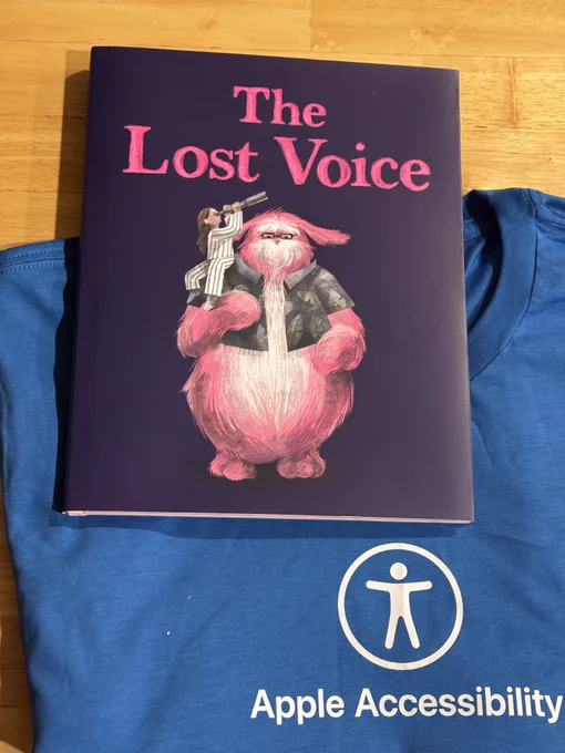 A physical copy of the book "The Lost Voice", and a blue shirt that says Apple Accessibility