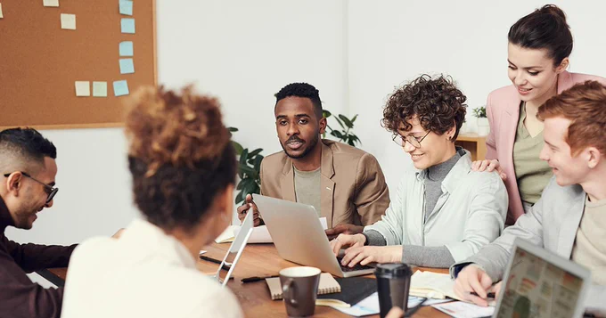 Eine Gruppe von Personen sitzen um einen Tisch mit ihren Laptops und diskutieren.