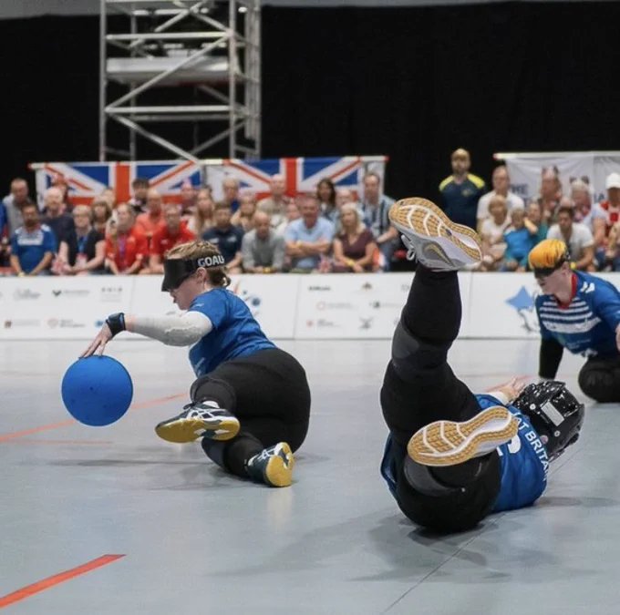 An action shot of me stopping a goalball with two teammates diving behind me and a crowd in the background.
