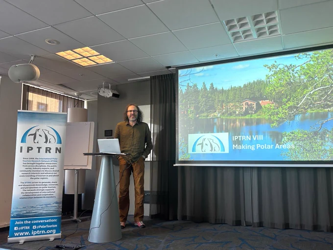 Professor Dieter Müller welcoming delegates to the 8th IPTRN conference in Luleå, Sweden.  Dieter is standing on a stage in front of the IPTRN banner and a background slide.