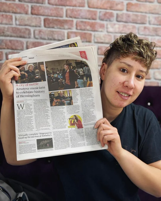 Jas holds up the Guardian article about Brum Rocks Live. The headline reads ‘A city of mettle - Amateur musicians to celebrate history of Birmingham’