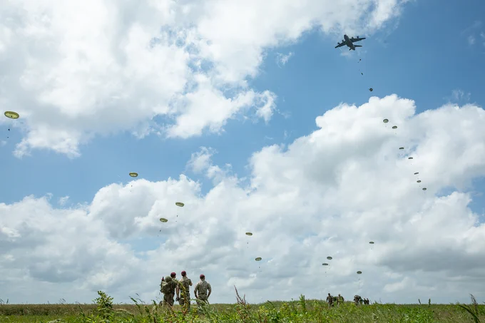 Paratroopers being dropped from A400M in the air, with personnel looking on on the ground.