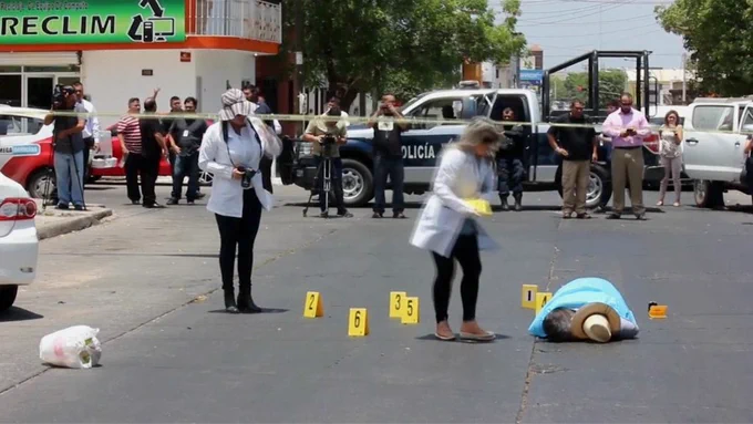 The body of journalist Javier Valdez lies in the street with police tape around as well as journalists stepping into the crime scene