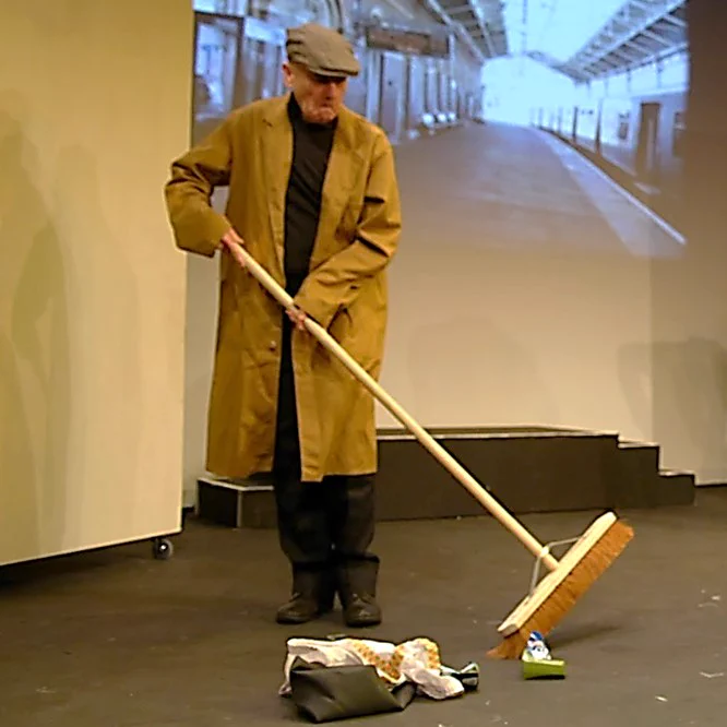 A character in Cheshire Cats. He is wearing a brown coat and using a long handled broom to sweep the floor.