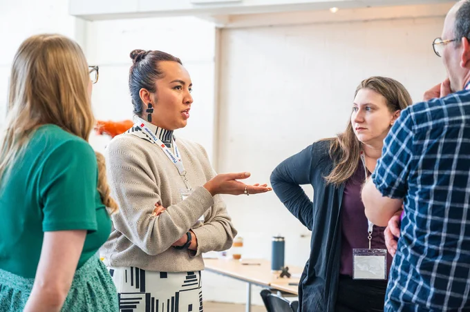 Alex Cabral from Grounded Solutions Network gestures with her palm up as she talks animatedly with her fellow Housing Breakthrough cohort members. The three people around her seem engaged as they listen attentively.