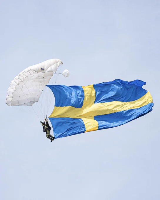 A Swedish paratrooper in the skies with the Sweden national flag during the Swedish Army's 500th anniversary celebration. Photographer: Jimmy Croona, Swedish Armed Forces