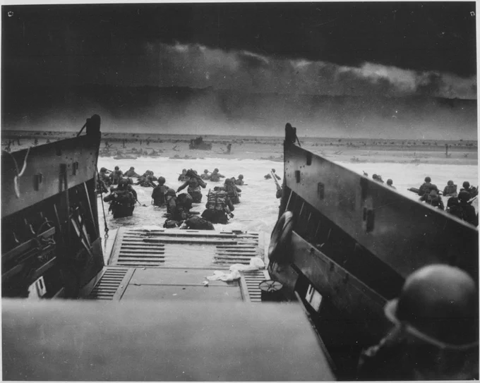 A black and white photograph of Allied ships descending upon Normandy.