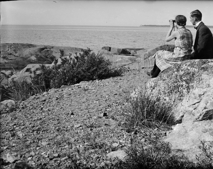 Black and white photo of two people sat on rocks, looking out to sea