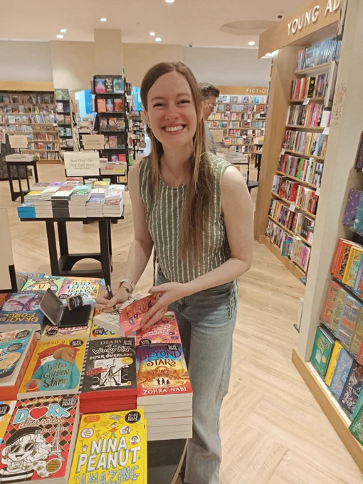 Fiona smiling at the camera and signing a stack of Freya's Gold books