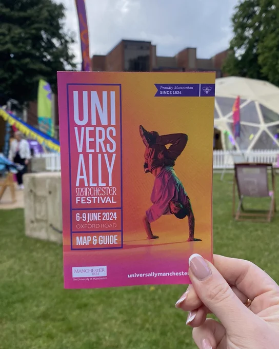 A photo of the front of a festival map for Universally Manchester Festival. In the background there are colourful flags and tents