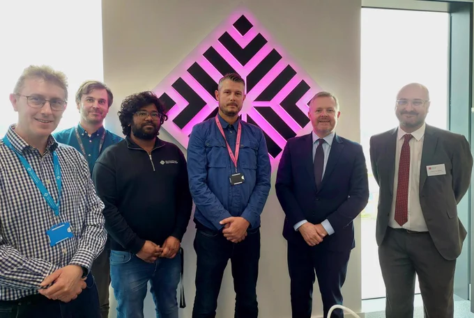 Jeremy Miles with Cyber Innovation Hub team in front of glowing logo