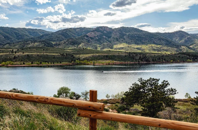 A boat leaves a wake behind it as it zooms along the shore of Horsetooth Reservoir under a light cloudy sky.