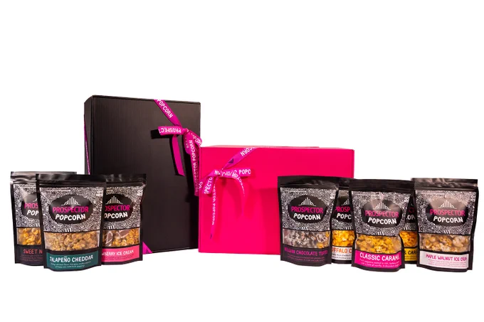 Eight assorted flavors of gourmet popcorn stand next to a pink and black gift box.