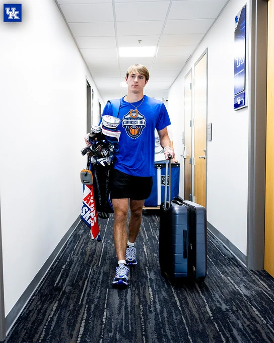 Travis Perry walking through the hallway with his golf bag and suitcase. 