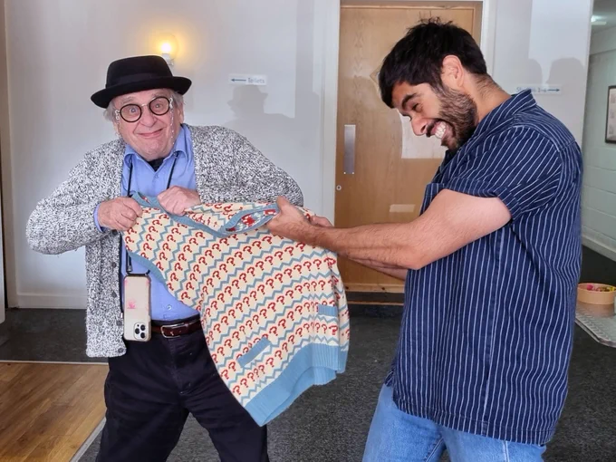 Actors Sylvester McCoy and Sacha Dhawan apparently fighting over the Seventh Doctor's trademark question mark jumper (as worn by both in Doctor Who). The jumper is stretched between as they each grip it and try to pull it toward themselves. Sylvester is looking toward the camera with a vexed expression on his face. Sacha is gritting his teeth and looking at the jumper.
(yes i stole the alt text from big finish)