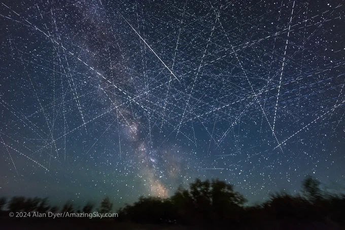 This is a stack of 560 two-second exposures, taken from 1:40 am to 2:10 am MDT on the night of June 4/5, about the time the sky was at its darkest. Even so, despite being near New Moon, the sky is blue from the perpetual twilight of a June night at my latitude. 

The lens was the Laowa 15mm wide open at f/2 on the Canon R6 at ISO 16,000, very high in order to record as much as possible in two seconds, to keep the satellites' trails on each frame as short as possible, and for the purpose of creating a time-lapse movie. The camera was on a tracker following the sky and stars, so they remain points, and the Milky Way shows up at center. The ground is blurred, though it comes from a blend of just 50 frames from the end of the sequence. 